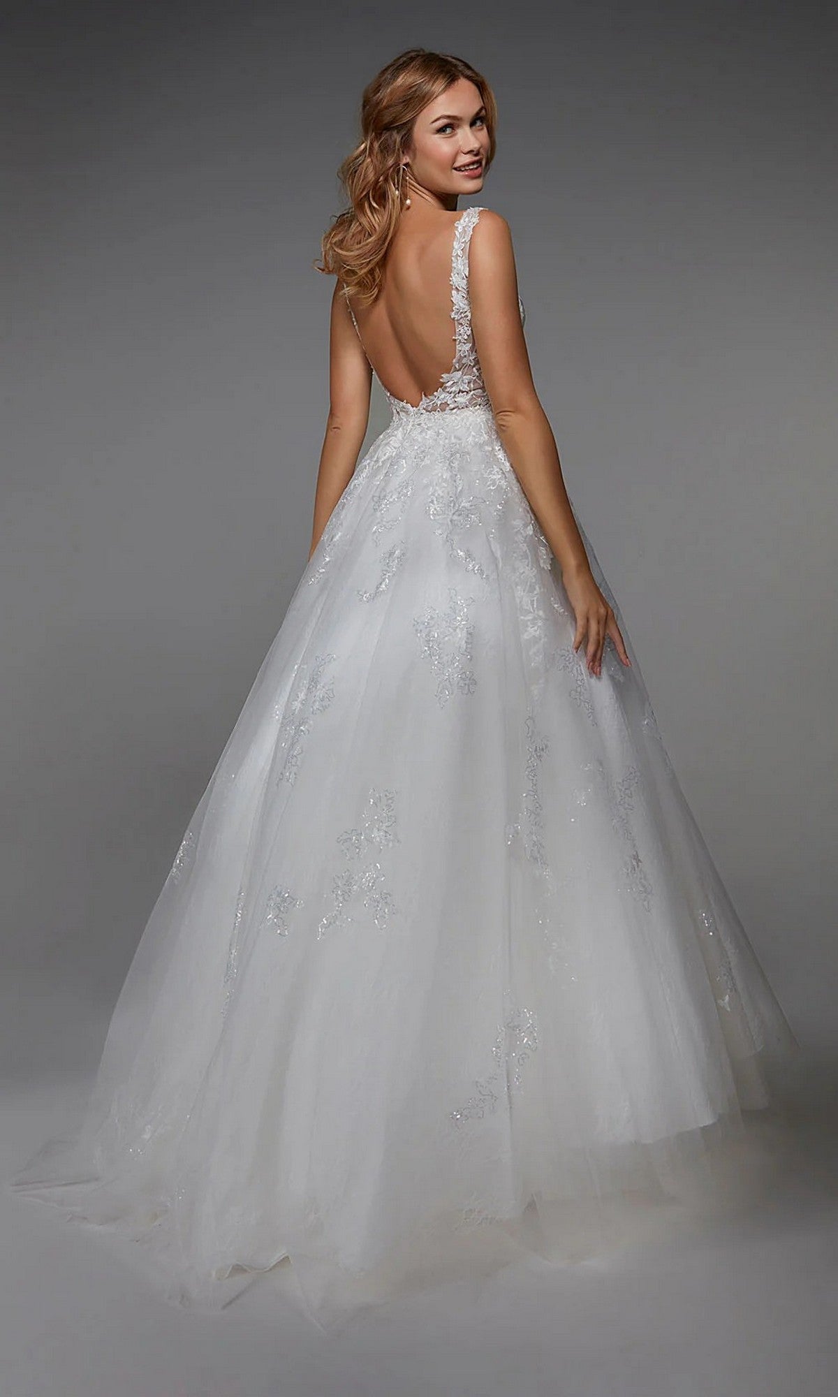 A woman, seen from behind, wears the sleeveless, backless Long White Dress: Alyce 7039 with delicate lace details, standing against a gray background.